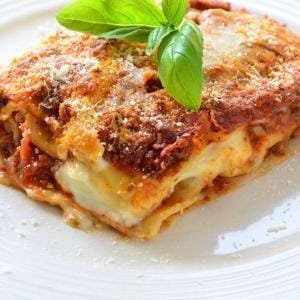 Orijinal İtalyan usulü kıymalı lazanya tarifi: Kat kat makarna, bolonez ve beşamel sos ile hazırlanmış, üzeri mozzarella peyniriyle kızarmış bir dilim lazanya servis tabağında sunuluyor.