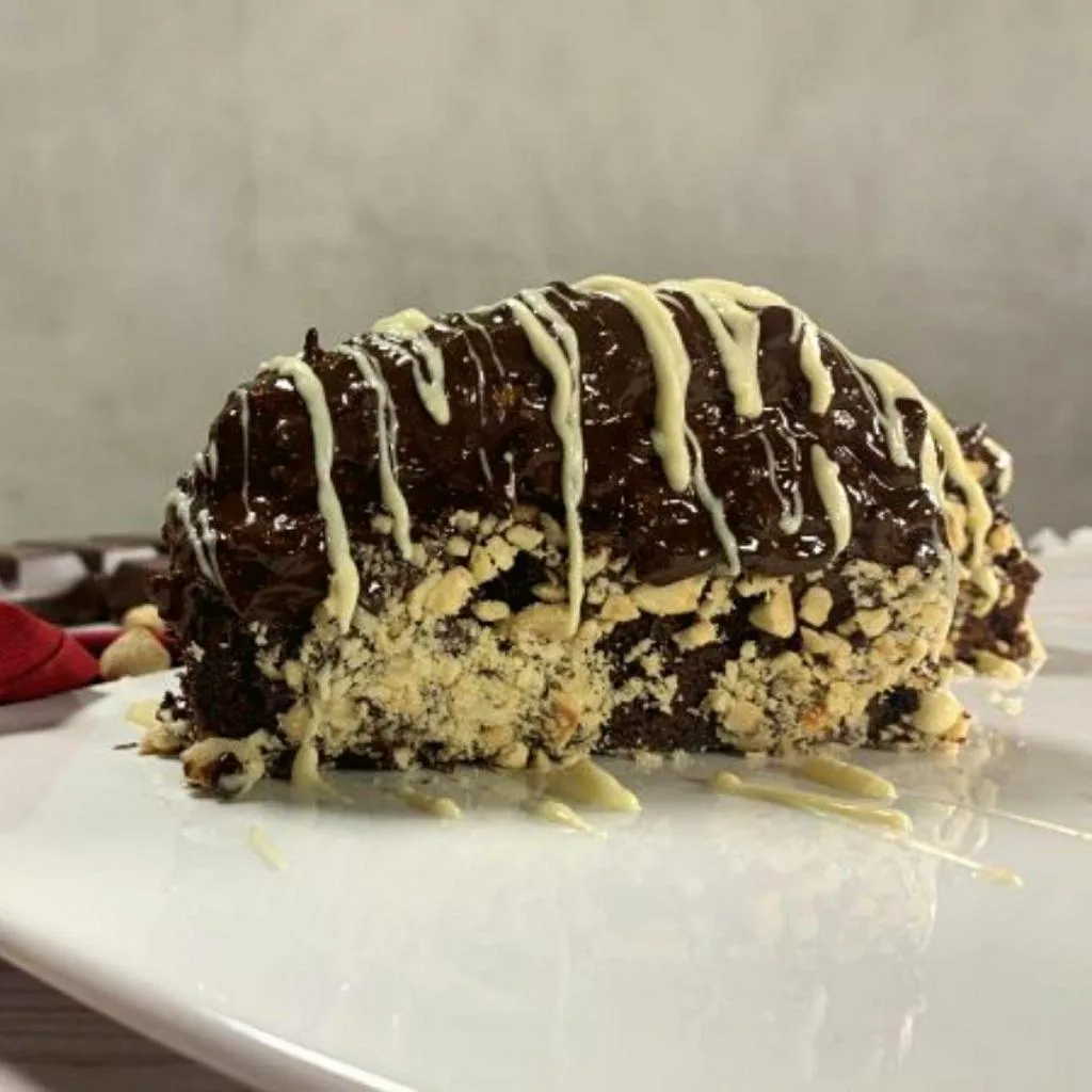 Çikolata kaplamalı, muzlu, fındık taneleriyle süslenmiş ev yapımı bir Malaga dilimi – içi krema dolgulu ve parlak çikolata şelalesiyle kaplı