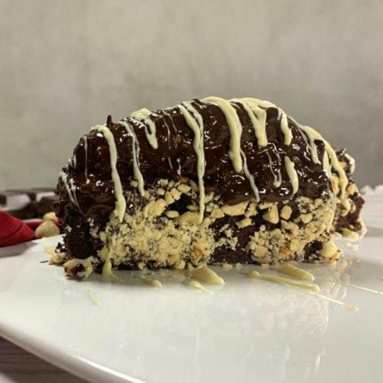 Çikolata kaplamalı, muzlu, fındık taneleriyle süslenmiş ev yapımı bir Malaga dilimi – içi krema dolgulu ve parlak çikolata şelalesiyle kaplı