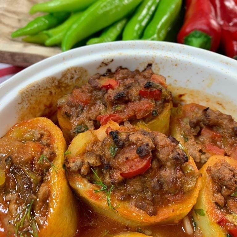 Fırından yeni çıkmış, kıymalı iç harcıyla doldurulmuş, üzeri sosla kaplanmış nefis Patates Dolması; altın rengi patates kabukları ve doyurucu görüntüsüyle iştah kabartan bir sunum.