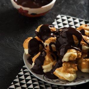 Altın rengi, hafifçe çıtır profiterol topları, içerisindeki ipeksi kıvamlı yoğun vanilyalı krema ile dolgun, üzerlerine akışkan ve parlak, koyu çikolata sosu bolca gezdirilmiş, her biri pastane usulü zarafet ve doğallıkla bezenmiş, karşı konulmaz bir tatlı şöleni.