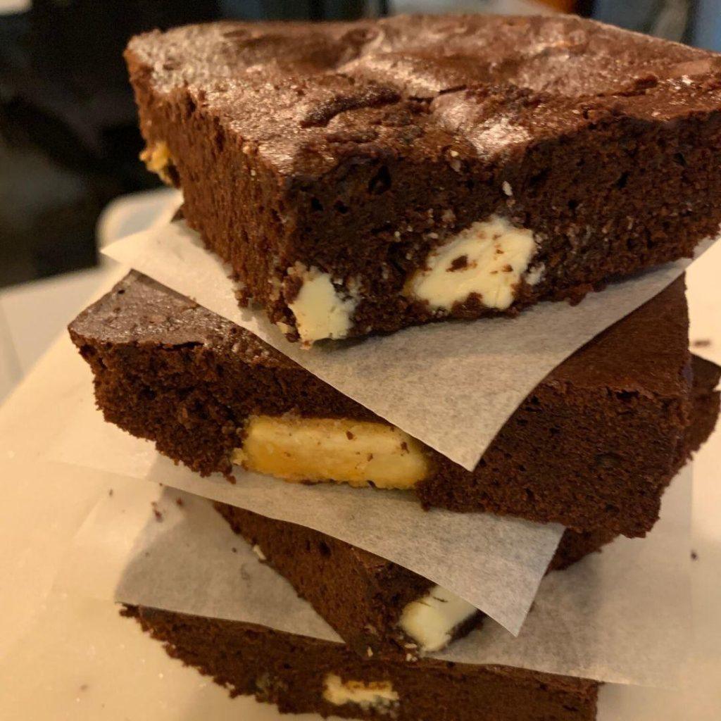 Beyaz Çikolatalı Brownie Tarifi : Bir tabakta, üzeri parlak ve çatlak, içinden erimiş beyaz çikolata parçaları görünen, ıslak dokulu brownie dilimi.