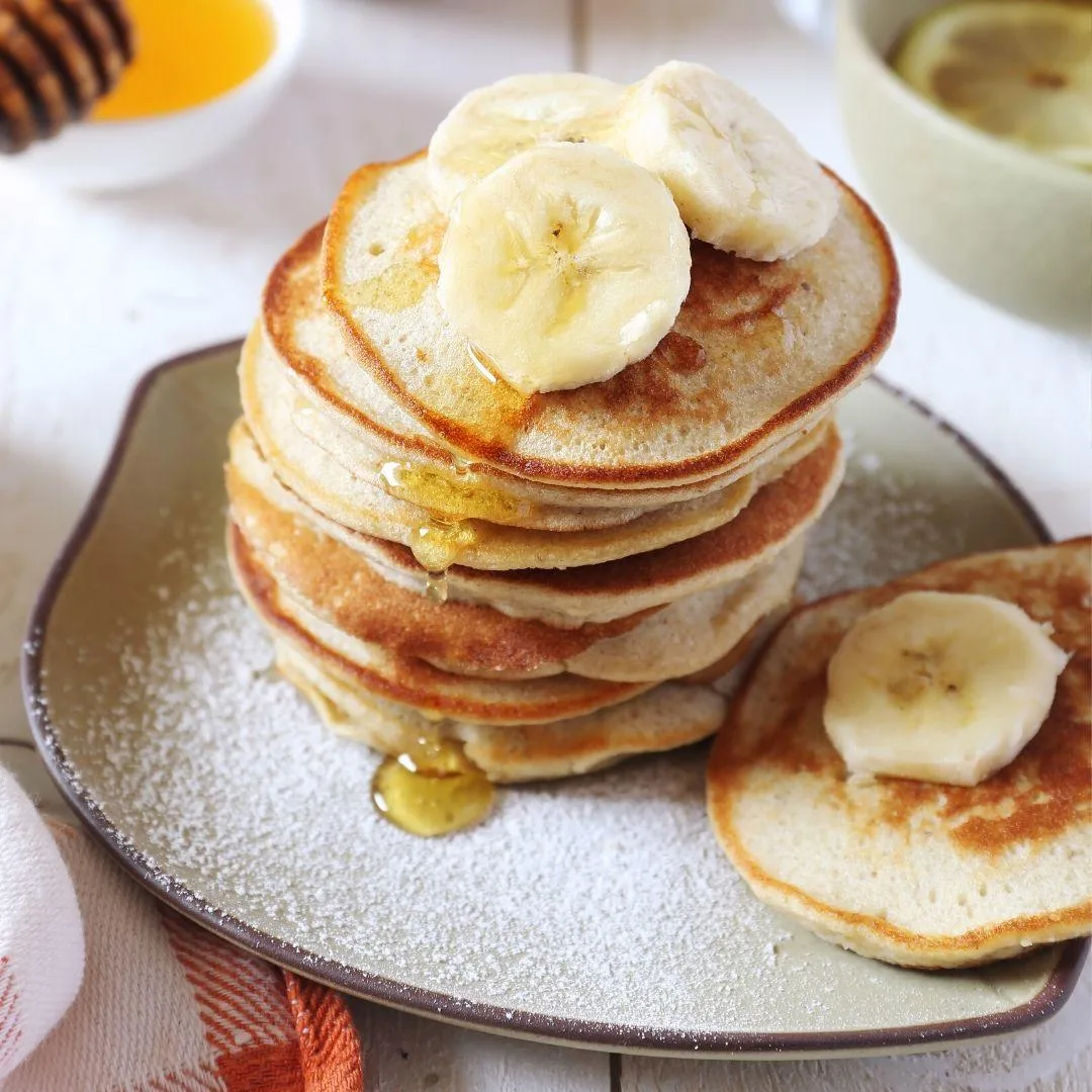 Glutensiz pancake tabakta üst üste dizilmiş, üzerinde taze çilek ve akçaağaç şurubu