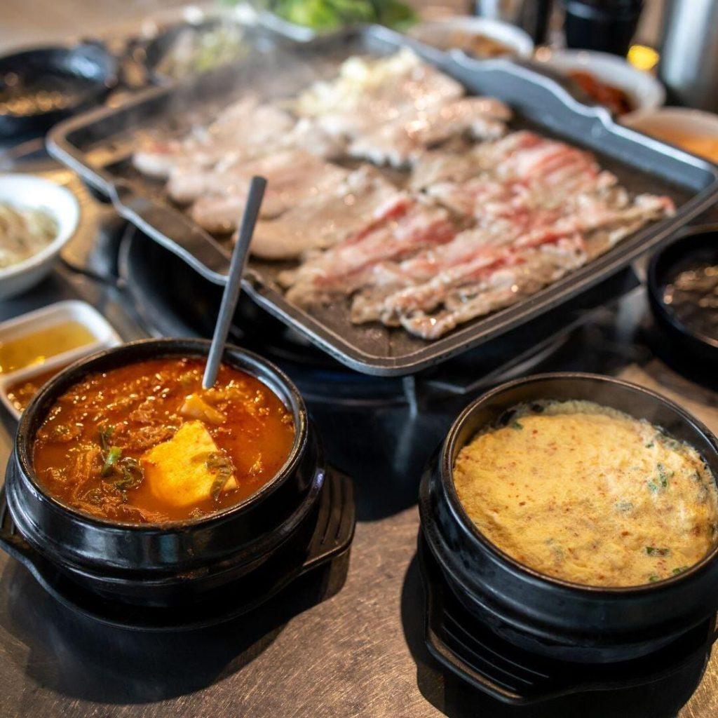 Samgyeopsal ızgarada; cızırdayan dilimlenmiş domuz eti, yanında marul ve ssamjang