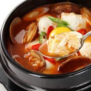 Sundubu-jjigae taş güveçte; gochugaru ile kızıl çorba, yumuşak tofu ve deniz ürünleri