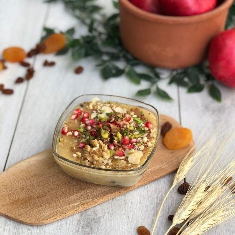 Aşure Tarifi: Cam kaselerde sunulmuş, üzeri parlak nar taneleri, ceviz, fındık ve tarçın gibi doğal malzemelerle zengin bir şekilde süslenmiş, tam kıvamında, iştah açıcı geleneksel aşure.