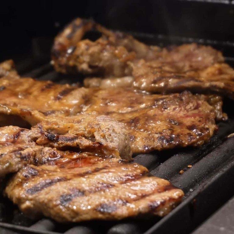 Elektrikli ızgarada mükemmel pişmiş, sosla parlayan, yanında taze baharatlarla servis edilen iştah açıcı soslu dana biftek sunumu