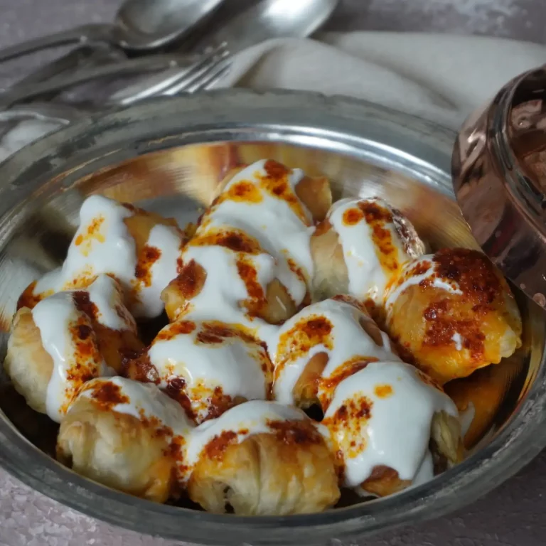 Milföyden Boşnak Mantısı Tarifi: Fırında altın renginde kızarmış, kat kat çıtır milföylerin üzerine bolca gezdirilmiş kıvamlı sarımsaklı yoğurt ve pul biberli kızgın tereyağı ile servis edilen iştah açıcı sunum.