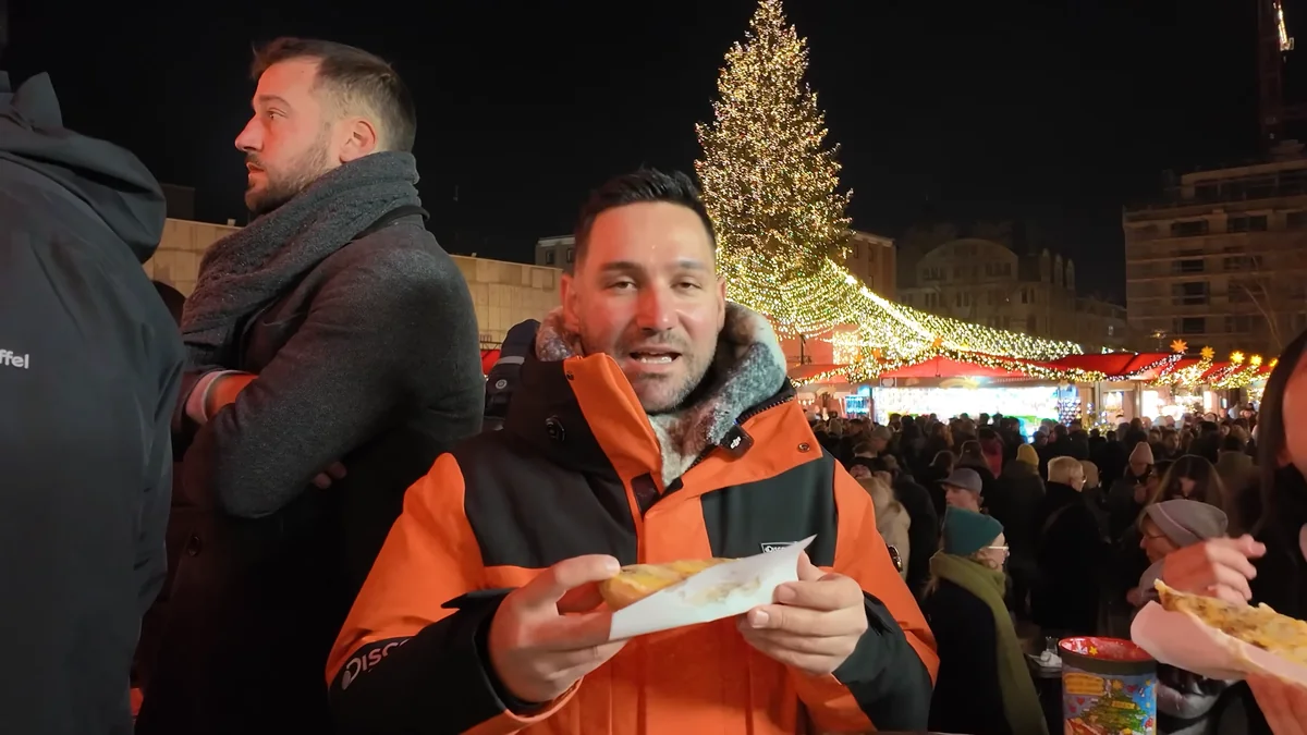 Halil tasting raclette at the Cologne Cathedral Christmas market with a lit Christmas tree behind