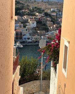 Symi Adası sokakları: Pembe begonviller arasından liman ve Sömbeki evleri manzarası.