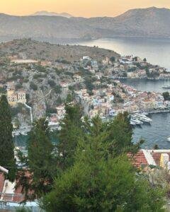 Symi Adası manzarası: Gün batımında liman, tekneler ve tepeye kurulu tarihi renkli evler.