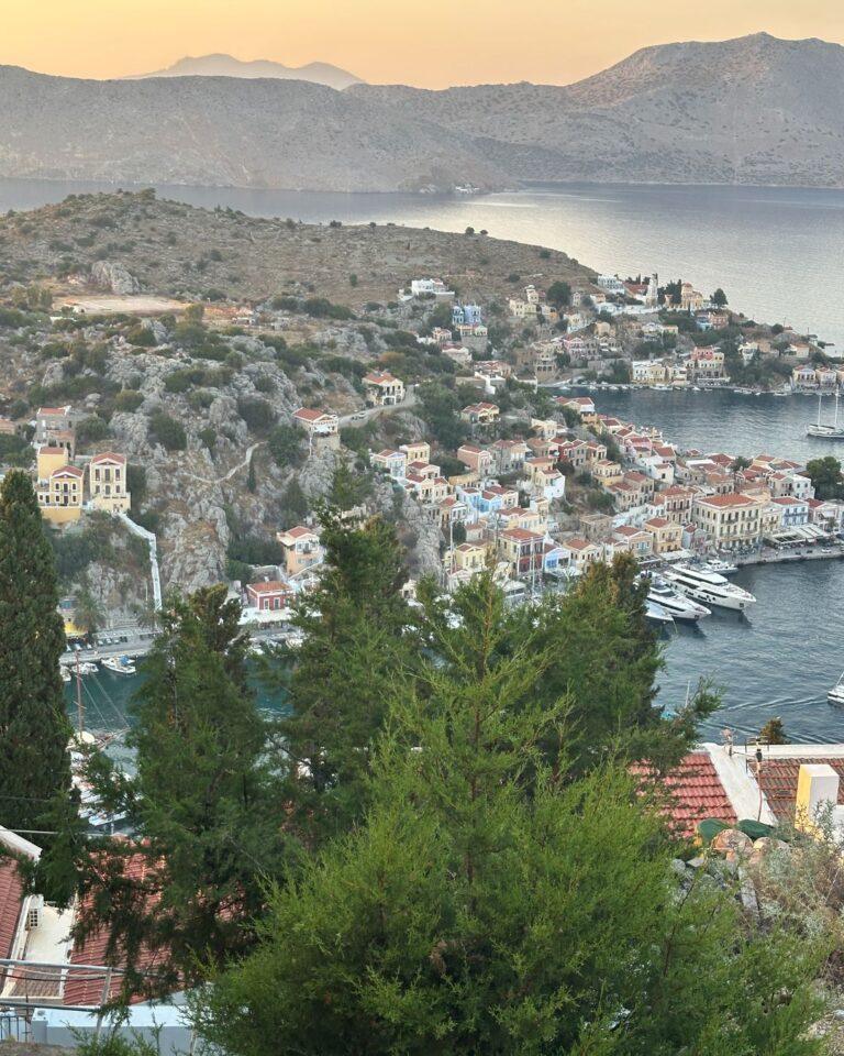 Symi Adası manzarası: Gün batımında liman, tekneler ve tepeye kurulu tarihi renkli evler.