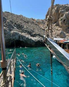 Symi Adası tekne turunda berrak turkuaz koylarda yüzen insanlar ve kayalık sahil manzarası.