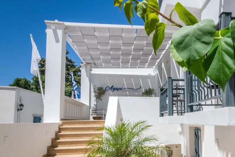 Agapi Hotel Tinos girişi: merdiven, beyaz pergola ve otelin tabelası