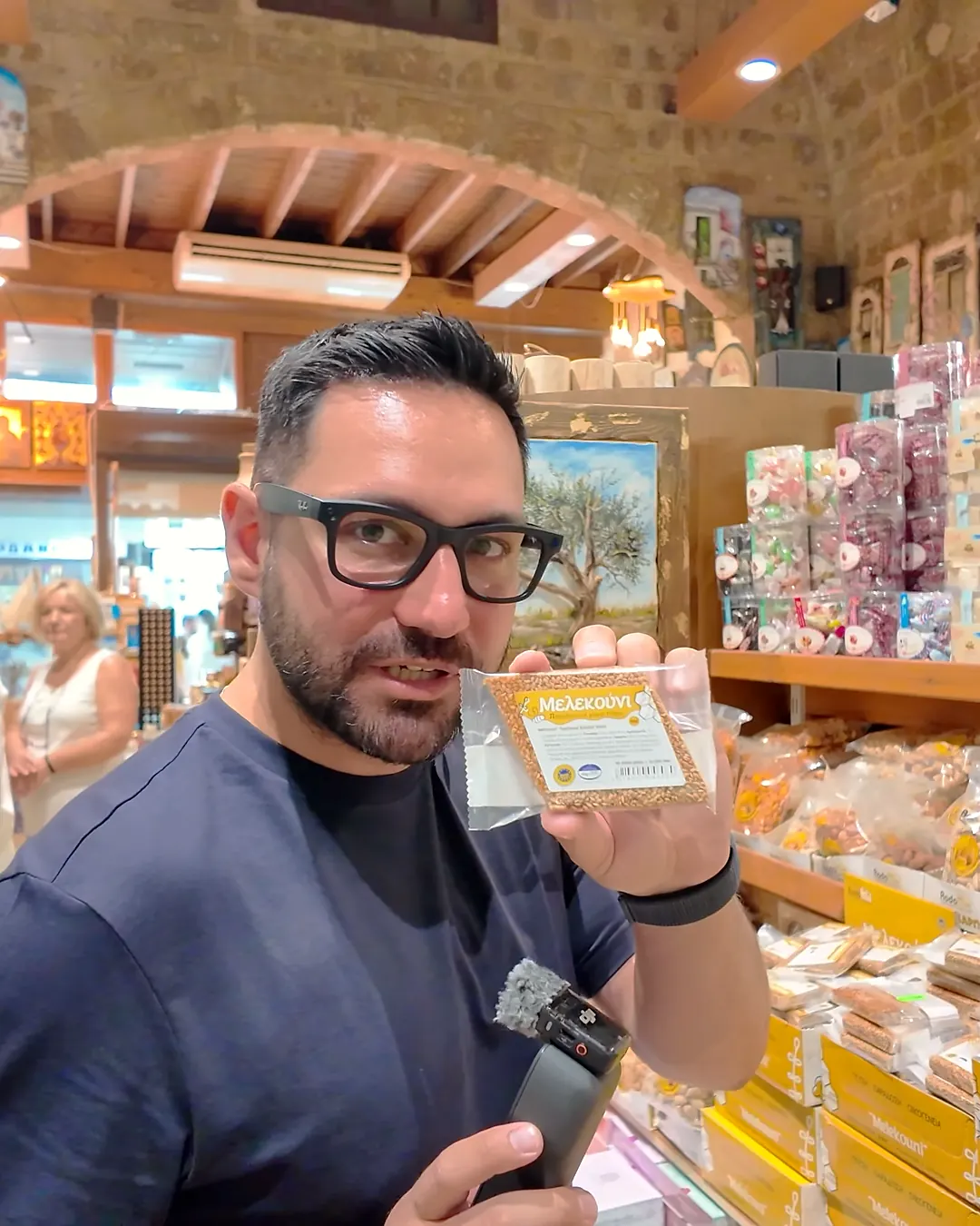 Rodos eski şehirdeki geleneksel tatlı dükkânında elde tutulan Melekouni paketi, arkada nougat ve bal ürünleri rafları