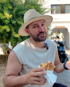 Rodos sokaklarında elde tutulan sıcak souvlaki pita dürüm, arkada gölgeli meydan ve scooterlar