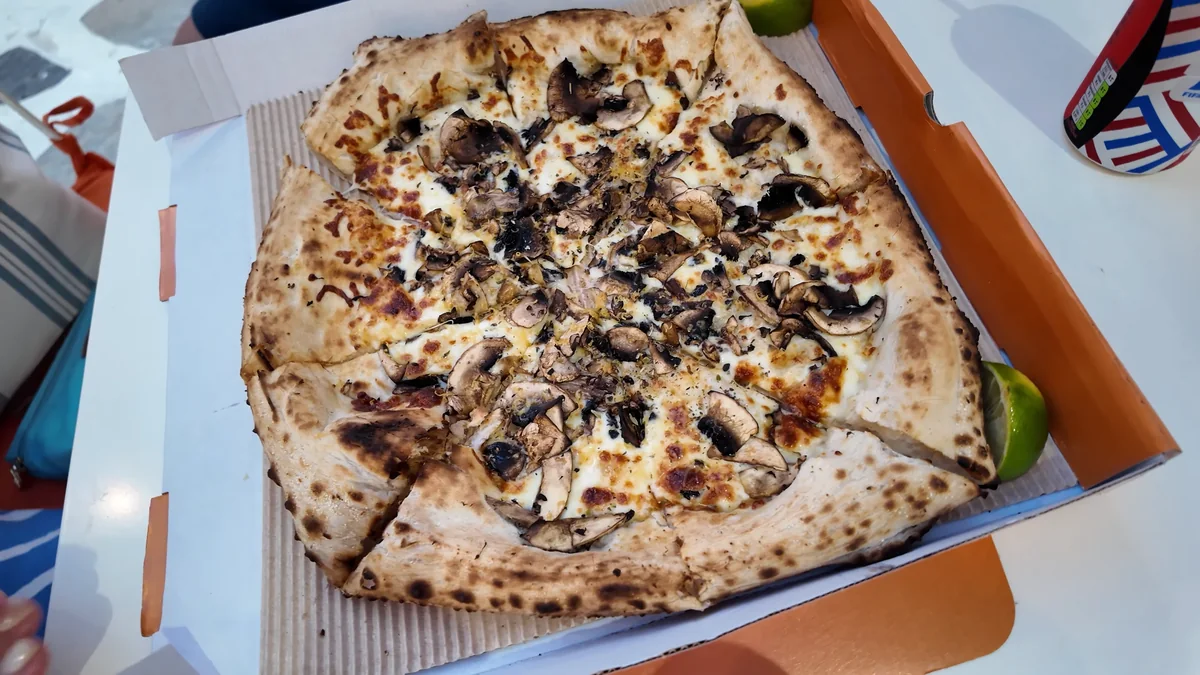 Tinos’ta Pizza Tales’in mantarlı Napoli usulü pizzası, kutuda ve yanında lime dilimi