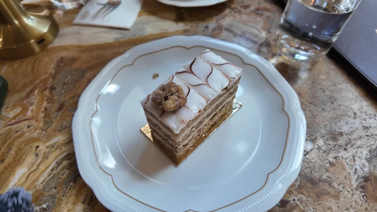 Budapeşte Café Gerbeaud’da mermer masada, altın kenarlı porselen tabakta katmanlı Macar pastası dilimi
