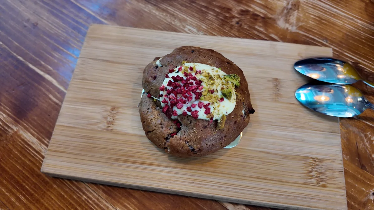 Budapeşte Cookie Beacon Brunch’ta ahşap tahtada servis edilen, üzeri kremalı ve antep fıstıklı dev kurabiye