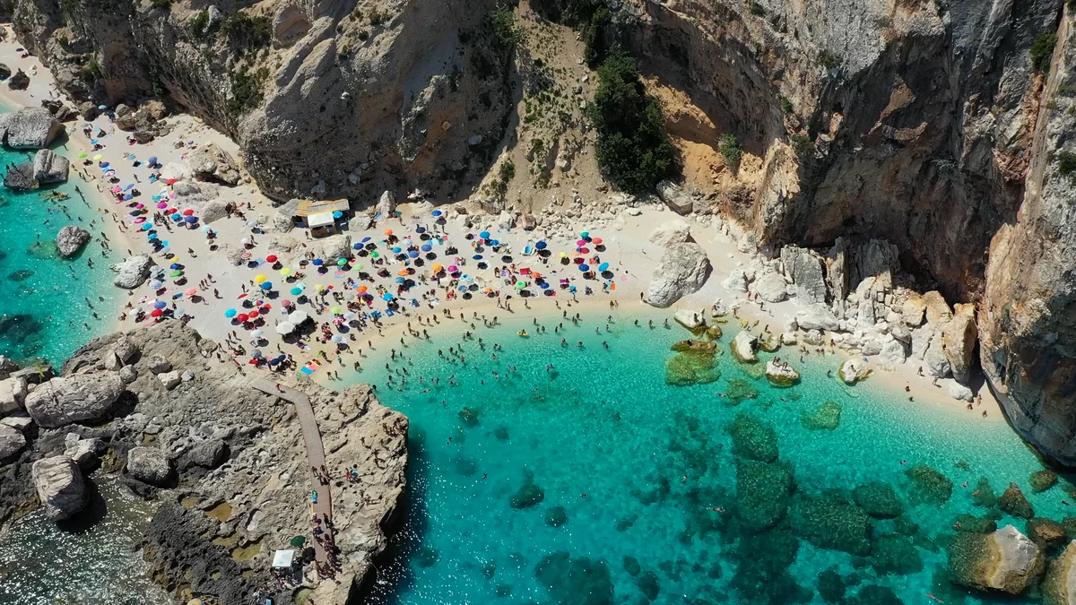 Baunei Cala Mariolu koyunda renkli şemsiyelerle dolu çakıl plaj ve turkuaz deniz
