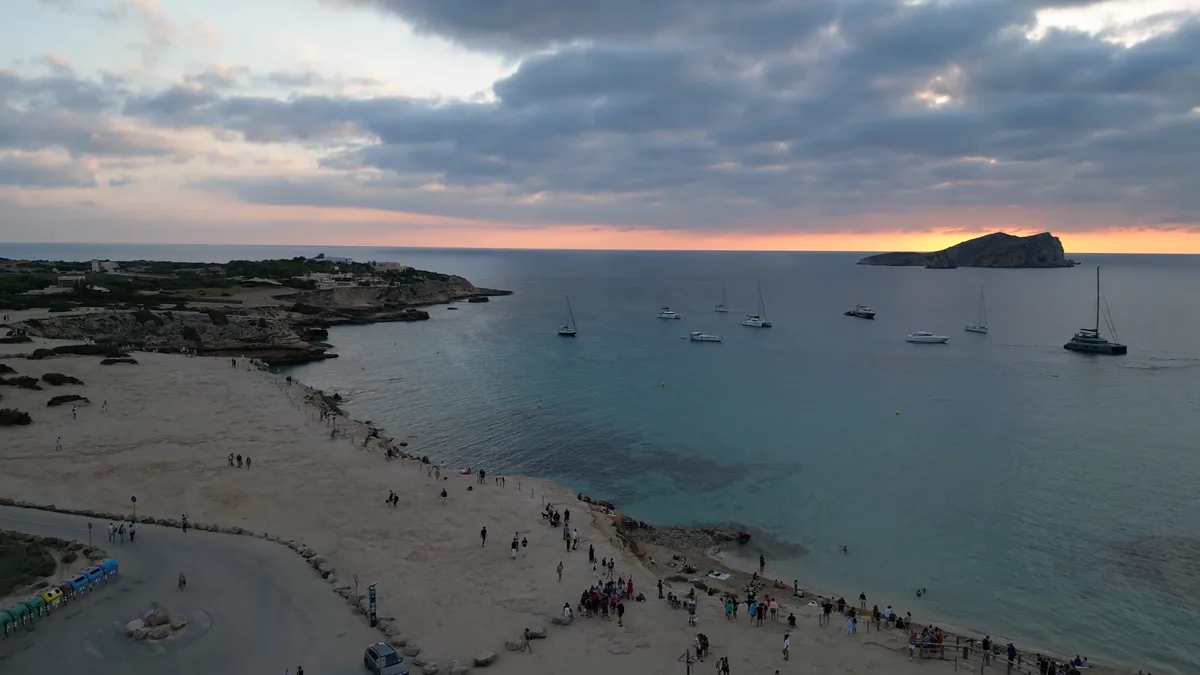 İbiza’da Cala Comte’de gün batımı: turuncu ufuk, karşıdaki ada ve demirlemiş tekneler