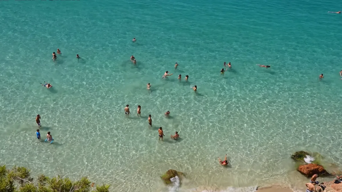 İbiza’da Cala Saladeta’nın berrak suyu: sığ turkuaz denizde yüzen insanlar