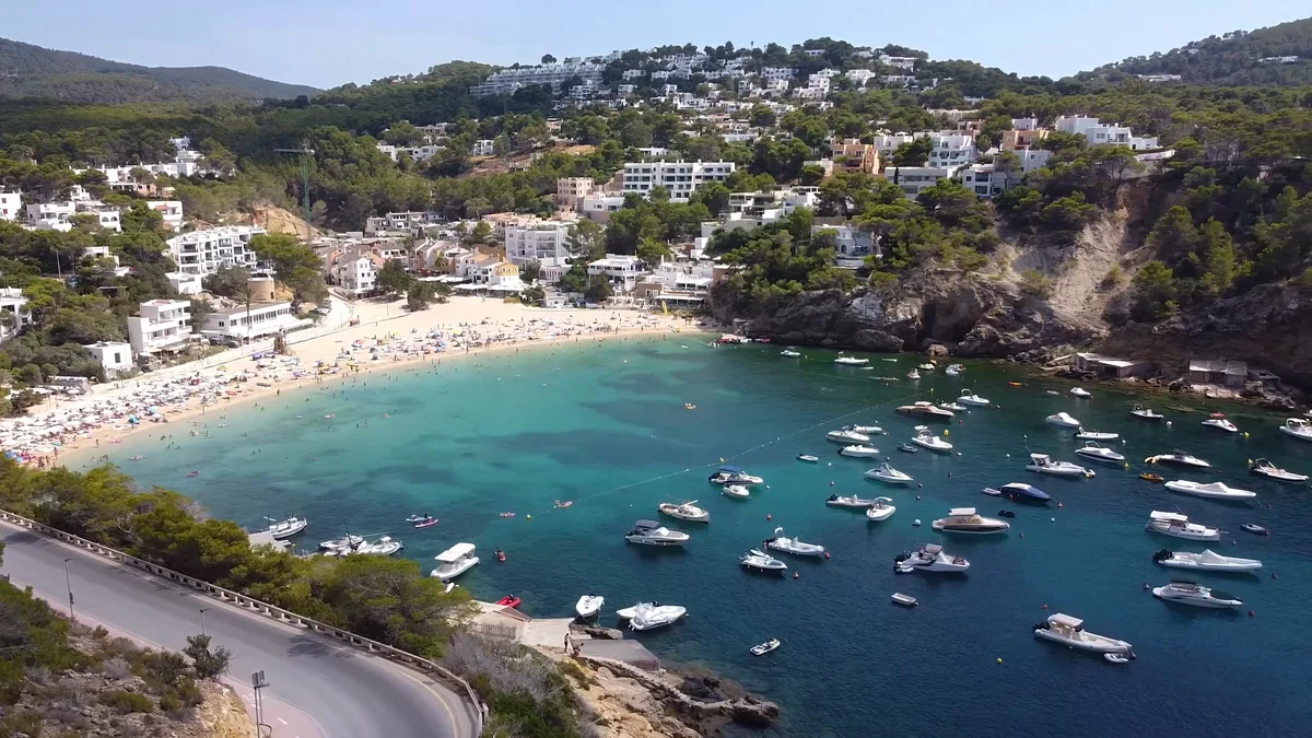 İbiza’da Cala Vadella koyu: kayalıkların koruduğu kumsal, turkuaz su ve demirlemiş tekneler