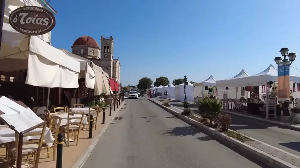 Egina sahilinde taverna masaları, tenteler ve kilise kubbesi