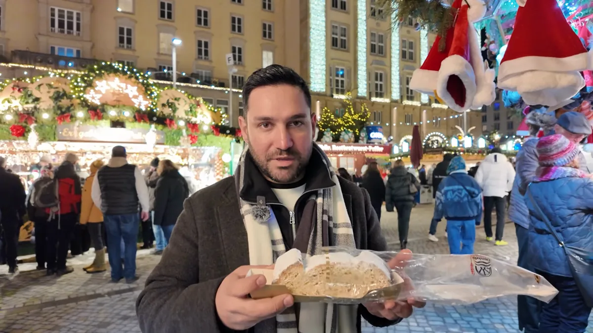 Halil holding a slice of almond Mandelstollen dusted with powdered sugar at the Dresden Christmas market