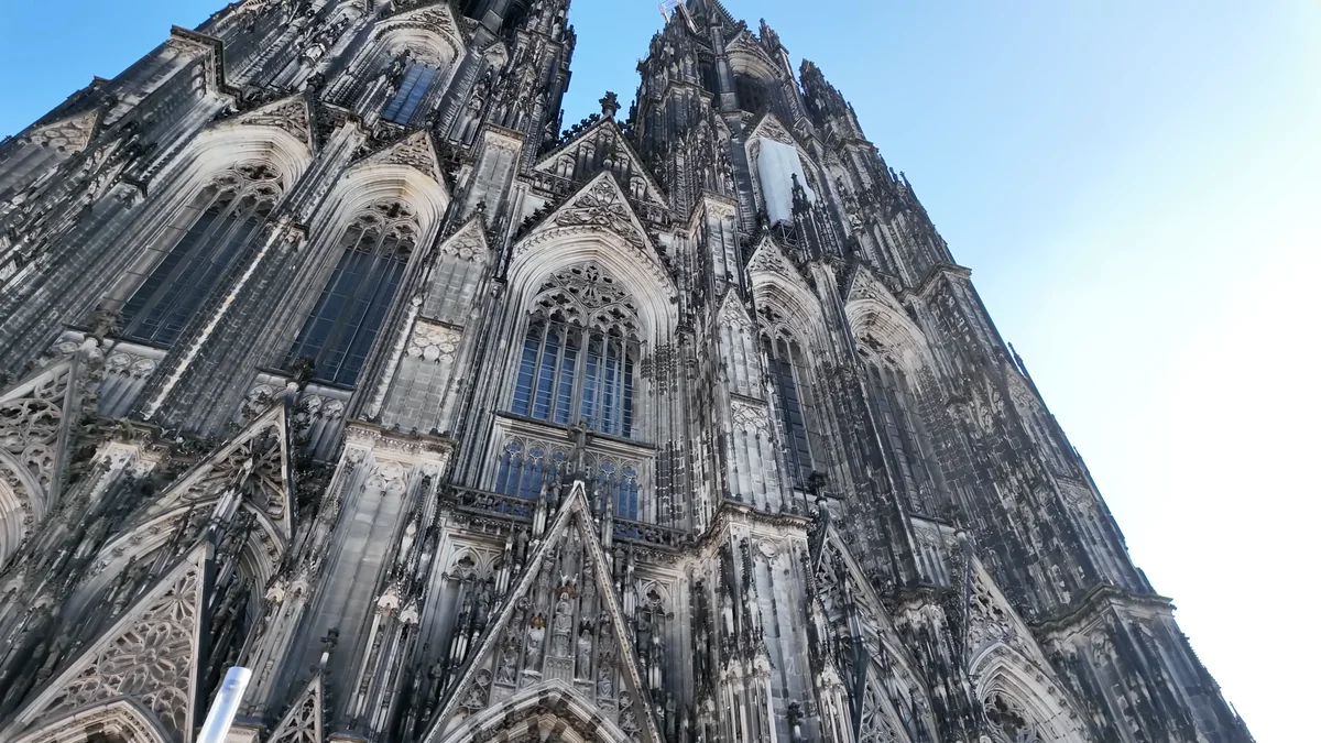 The Gothic west facade and twin towers of Cologne Cathedral seen from below against a blue sky