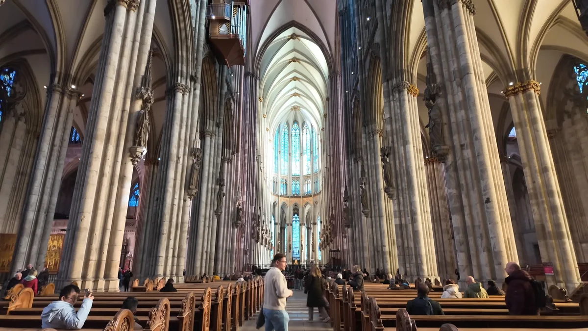 Inside Cologne Cathedral: the nave between tall Gothic pillars and the apse with stained glass windows